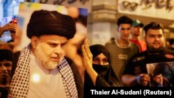 Seorang perempuan memegang foto pemimpin gerakan Sadr Moqtada al-Sadr, saat para pendukungnya merayakan setelah hasil awal pemilihan parlemen Irak diumumkan di Baghdad, Irak 11 Oktober 2021. (Foto: REUTERS/Thaier Al-Sudani)