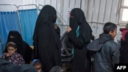 FILE - Two women, center, reportedly wives of Islamic State (IS) group fighters, wait with other women and children at a camp of al-Hol in al-Hasakeh governorate in northeastern Syria, Feb. 7, 2019.