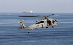 FILE - MH-60S helicopter hovers in the air with an oil tanker in the background as the USS John C. Stennis makes its way to the Gulf through the Strait of Hormuz, Dec. 21, 2018.