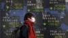 FILE - A pedestrian walks past an electronic board showing the stock market indices of various countries outside a brokerage in Tokyo, Japan, Feb. 3, 2016. 