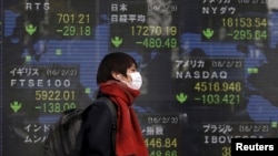 FILE - A pedestrian walks past an electronic board showing the stock market indices of various countries outside a brokerage in Tokyo, Japan, Feb. 3, 2016. 