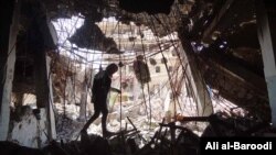 FILE -- Tahany Saleh walks through a pile of debris at the gate of Mosul University’s Central Library as she works with her volunteer team to rescue books in the burned building, Mosul, Iraq, May 2017. 