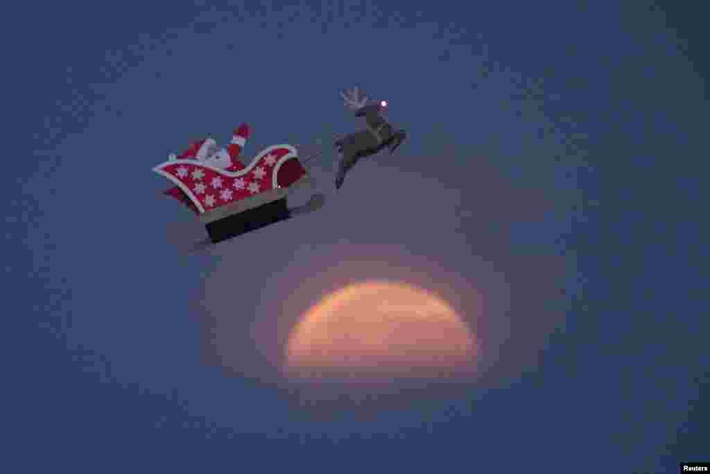 美国加利福尼亚州卡尔斯巴德，朦胧月色下，一艘10英尺长的遥控飞行的圣诞老人和驯鹿雪橇飞翔。（2017年12月3日）