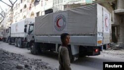 FILE - A boy stands as an aid convoy of Syrian Arab Red Crescent drives through the town of Douma, Eastern Ghouta, near Damascus, Syria, March 5, 2018.