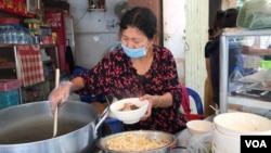 អ្នកស្រី ពិន នារី លក់​គុយទាវ​ឆា និង​បបរ​នៅ​កែង​ផ្លូវ​មួយ​ជិត​ស្នាក់ការ​សង្កាត់​ចតុមុខ ដែល​បាន​ផ្អាក​ជាង​មួយ​ខែដោយសារ​ជំងឺ​កូវីដ​១៩ កំពុង​បើក​លក់​ឡើង​វិញ នៅថ្ងៃទី២៧ ខែមេសា ឆ្នាំ២០២០។ (កាន់ វិច្ឆិកា/VOA)