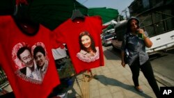 FILE - A pro-government supporter passes t-shirts with portraits of Prime Minister Yingluck Shinawatra and her self-exiled brother Thaksin at the gate of the National Anti-Corruption Commission office in Bangkok, Thailand, Thursday, Feb. 27, 2014.