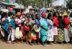 FILE - Women queue for a planned distribution of food for those suffering from the impact of the coronavirus pandemic, at a site in the Kibera slum of Nairobi, Kenya, April 10, 2020.