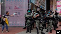 Policija u opremi za razbijanje demonstracija stražari, dok žena pokušava da pređe ulicu u centru Hong Konga, 27. maja 2020.