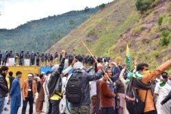 FILE - Pakistani policemen stand over shipping containers on a street leading toward the border as supporters of Jammu Kashmir Liberation Front gather during a protest march against India, in Jaskool, in Pakistan-controlled Kashmir, Oct. 7, 2019.