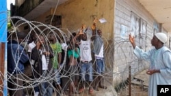 A man, right, working for a humanitarian group, throws water in a small bag to West Point residents behind the fence of a holding area, as they wait for a second consignment of food from the Liberian Government to be handed out, at the West Point area, near the central city area of Monrovia, Liberia, Friday, Aug. 22, 2014. Two new cases of Ebola have emerged in Nigeria and, in an alarming development, they are outside the group of caregivers who treated an airline passenger who arrived with Ebola and died, Health Minister Onyebuchi Chukwu said Friday.(AP Photo/Abbas Dulleh)