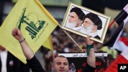 Seorang pendukung Hezbollah memegang foto tokoh revolusioner Iran Ayatollah Khomeini (kiri) dan pemimpin tertinggi di Iran Ayatollah Ali Khamenei (kanan) dalam aksi unjuk rasa yang dipimpin oleh Hezbollah di Beirut, Lebanon, pada 17 April 2015. (Foto: AP/Bilal Hussein)