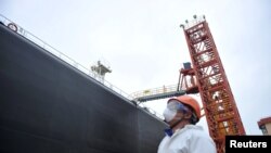 A dock worker wearing a face mask to guard against coronavirus disease (COVID-19) looks at a tanker unloading crude oil at a port in Qingdao, Shandong province, China, March 26, 2020.