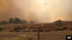 In this photo provided by Vince O'Daye, a helicopter flies over plumes of smoke from a wildfire in the community of Sutcliffe, about 35 miles north of Reno, Nevada, July 30, 2016.