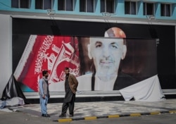 Afghan men stand next to a torn poster of Afghan President Ashraf Ghani at the Kabul airport in Kabul on August 16, 2021.