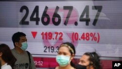 People wearing face masks walk past a bank's electronic board showing the Hong Kong share index in Hong Kong, Oct. 28, 2020.