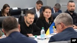 Ukrainian President Volodymyr Zelenskyy, center left, listens while visiting the Scranton Army Ammunition Plant in Scranton, Pennsylvania, Sept. 22, 2024. Seated next to Zelenskyy is Ukraine's Ambassador to the U.S. Oksana Markarova. (Sgt. 1st Class Curt Loter/U.S. Army via AP)