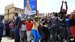 FILE - Police officers watch as crowds of people gather outside a police station in the Diepsloot area, north of Johannesburg, South Africa.