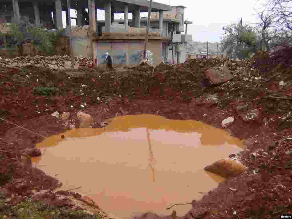 A woman walks near a crater caused by missiles fired by a Syrian Air Force fighter jet near Idlib, January 15, 2013.
