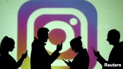 In this file photo, silhouettes of mobile users are seen next to a screen projection of the Instagram logo in this picture illustration taken March 28, 2018. (REUTERS/Dado Ruvic/Illustration/File Photo)