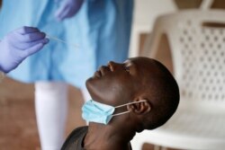 FILE - A health care worker prepares to collect a swab sample from a man during mass testing for the coronavirus in the Kibera slums of Nairobi, Kenya, Oct. 17, 2020.