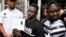 Malian migrant Mamoudou Gassama, center, with his older brother at right, holds his temporary residence permit after receiving it at the Prefecture of Bobigny, northeast of Paris, May 29, 2018. 