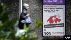 A woman walks past a campaign poster against toughening gun laws in Switzerland. It reads in French, "Yesterday banking secrecy, today shooting ... and tomorrow? Let's stop the spiral!" May 13, 2019, in Geneva.