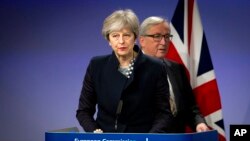 Presiden Komisi Uni Eropa, Jean-Claude Juncker (kanan) berjalan di belakang PM Inggris, Theresa May di Markas Besar Uni Eropa di Brussels, 4 Desember 2017. (Foto: dok). 