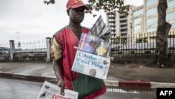Un marchand de journaux cherche des clients à un lampadaire à Libreville le 29 août 2016 tout en affichant des journaux locaux rapportant le résultat des élections présidentielles au Gabon.