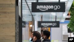 Two people wearing masks walk near an Amazon Go store in downtown Seattle, April 30, 2020.