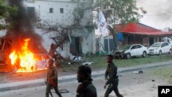 Wadansu jami'an tsaro suna wucewa gaban shagon da aka kona a Mogadishu, Somalia, May, 8, 2017. 