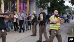 ប៉ូលិស​ដើរ​អម​មនុស្ស​ដែល​កំពុង​ចាក​ចេញ​ពី​ផ្សារ​ទំនើប​ Olympia ក្នុង​ទីក្រុង​មុយនិចភាគ​ខាង​ត្បូង​ប្រទេស​អាល្លឺម៉ង់ កាល​ពី​ថ្ងៃទី​២២ ខែ​កក្កដា បន្ទាប់​ពី​មាន​ការ​បាញ់​ប្រហារ​នៅ​ទី​នោះ។