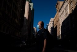 A man wearing a face mask walks across the street in Los Angeles, Friday, Aug. 7, 2020.
