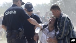 Macedonian police officers help a dehydrated migrant at the border from Greece to Macedonia, near southern Macedonian town of Gevgelija, on Monday, Aug. 31, 2015. (AP Photo/Boris Grdanoski)