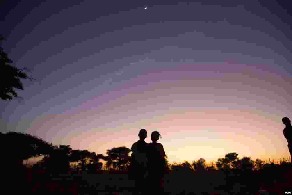 Children stand under a crescent moon as night falls in Tunguli village, Nuba Mountains. (Adam Bailes/VOA News)