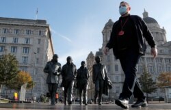 A man wearing a face mask walks past a statue of the Beatles, as new measures across the region are set to come into force in Liverpool, England, Oct. 14, 2020.