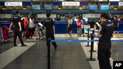 In this July 6, 2018, photo, Chinese security personnel watch as travelers check in for flights at the American Airlines check-in counters at the Beijing Capital International Airport in Beijing. (AP Photo/Mark Schiefelbein)