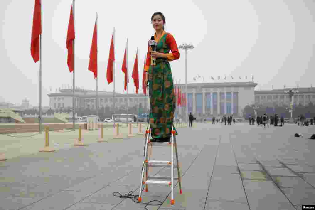 2018年3月3日，中国人民政治协商会议在北京开幕之前，在人民大会堂外的空荡荡的天安门广场，一位记者站在梯子上做报道。在人民大会堂开重要大会时，人民大会堂外面的广场经常是戒备森严，没有多少人民。当天北京雾霾严重，PM2.5指数超过200，非常不利于健康。看来今年当局并没有刻意营造&ldquo;两会蓝&rdquo;。