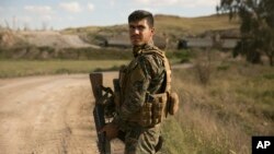 Seorang tentara Pasukan Demokratik Suriah berjaga saat truk-truk yang membawa anggot kelompok militan ISIS dan keluarganya menyerah di Baghuz, Suriah, dan pindah ke kamp, 19 Maret 2019. 