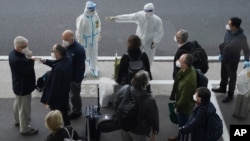 បុគ្គលិក​ម្នាក់ ​នៅក្នុង​ឈុតការពារ បាន​ចង្អុល​បង្ហាញ​ផ្លូវ​ដល់​សមាជិក​នៃ​ក្រុម​ដែល​ដឹកនាំ​ដោយ​អង្គការ​សុខភាព​ពិភពលោក (WHO) ពេល​ពួកគេ​ទៅ​ដល់​អាកាសយានដ្ឋាន​ក្នុង​ទីក្រុង​វូហាន ខេត្តហ៊ូប៉ី ដែល​នៅ​ភាគកណ្តាល​នៃ​ប្រទេសចិន នៅ​ថ្ងៃព្រហស្បតិ៍ទី១៤ ខែមករា ឆ្នាំ២០២១។