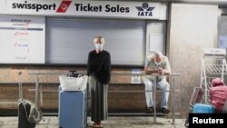 Passengers wait for confirmation of flights outside the Swissport Ticket Sales counter as several airlines stopped flying out of South Africa, amidst the spread of the new Omicron variant at O.R. Tambo International Airport in Johannesburg, South Africa, 