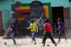FILE - Children play soccer next to a defaced portrait of former Zimbabwean President Robert Mugabe in Harare, Sept. 6, 2019.