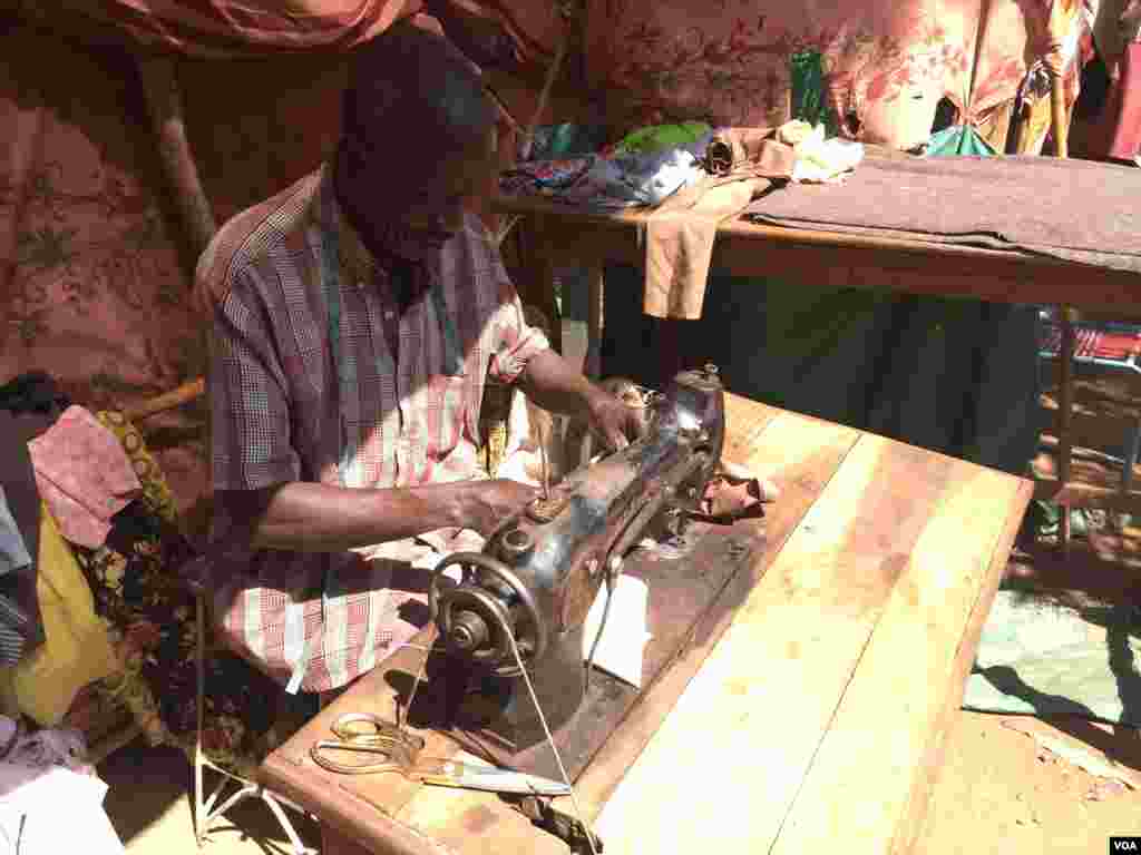 Tailor Adam Edman Idriss working in a small shelter at the St. Mary Help of Christians Cathedral in Wau, Western Bahr el Ghazal, South Sudan. Idriss lives on the church compound, with more than approximately 8,500 other IDPs, Dec. 8, 2016. (VOA/Jill Craig)