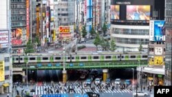 This general view shows people crossing the street as trains leave nearby Shinjuku station in Tokyo on June 17, 2021.