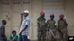 FILE - In this Saturday, Feb. 20, 2016 file photo, a man walks past listening to news on a portable radio as military police deploy, shortly after the election result was announced, and social media had been blocked, in downtown Kampala, Uganda. 