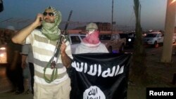 A fighter of the Islamic State of Iraq and the Levant (ISIL) holds a weapon while another holds a flag in the city of Mosul, June 23, 2014. 