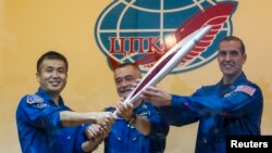 International Space Station (ISS) crew members, (L to R) Japanese astronaut Koichi Wakata, Russian cosmonaut Mikhail Tyurin and U.S. astronaut Rick Mastracchio, pose with the torch of the 2014 Sochi Winter Olympic Games, at the Baikonur cosmodrome, Nov. 6, 2013.