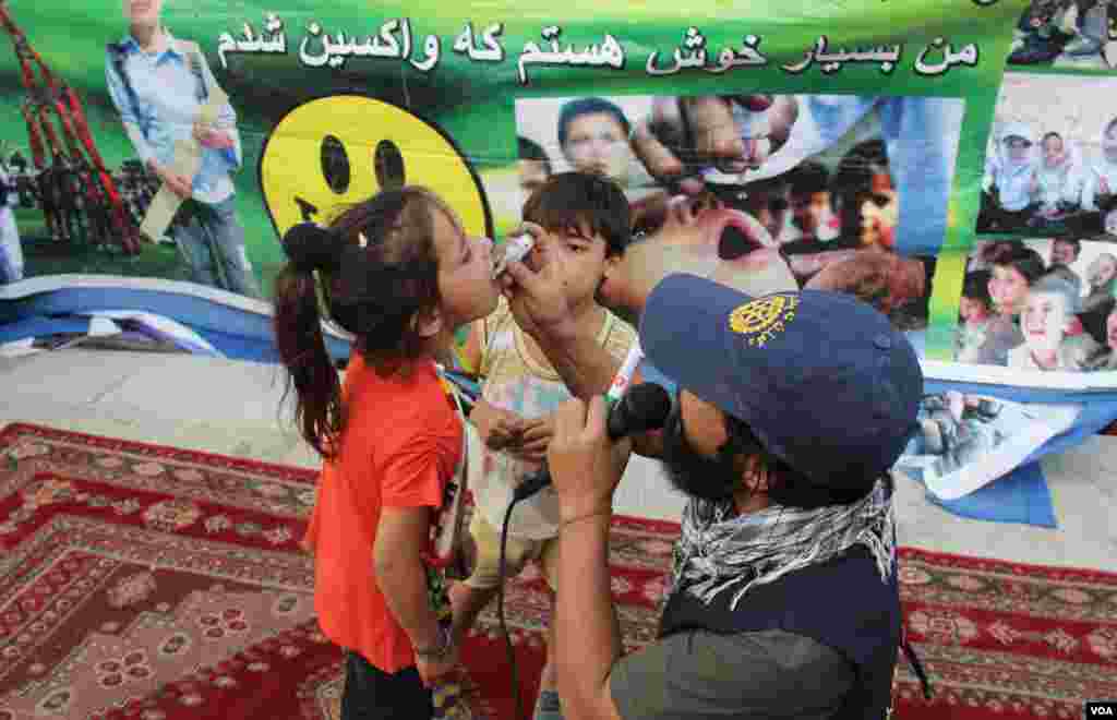 کارمند صحی در حال چکاندن قطره واکسین پولیو به دهان یکی از اطفال&nbsp;