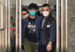 A Hong Kong university student is escorted by police officers after a home search on August 18, 2021. Four students were arrested on suspicion of promoting terrorism after publicly mourning a man who stabbed a police officer and then killed himself in July 2021.