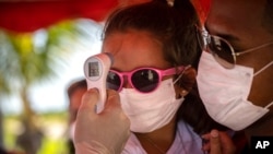 A little girl wearing a face mask amid the new coronavirus pandemic gets her temperature taken at a police checkpoint, at the entrance to the province of Havana, Cuba, Monday, Aug. 10, 2020. Cuban authorities on Monday re-imposed measures aimed at…