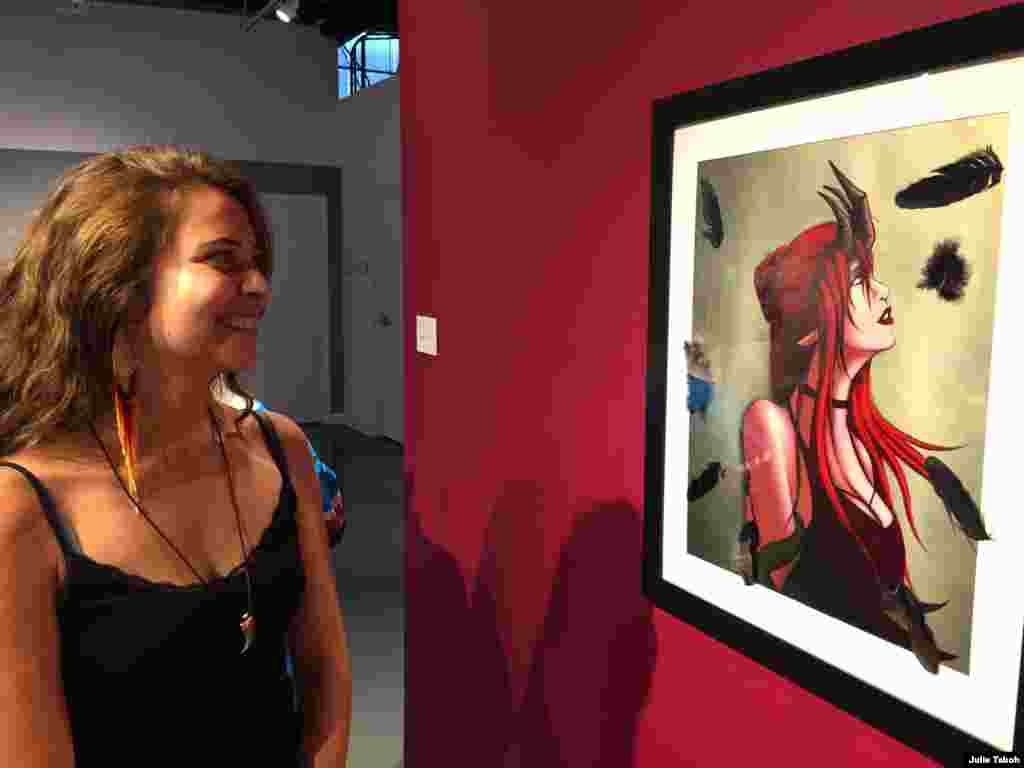 International student Erika Knecht poses with one of her favorite pieces of art, Mollyanna Sabori’s digital painting “Black Feathers,” on display at the Balzer Contemporary Edge Gallery on the IAIA campus, Santa Fe, N.M., Oct. 9, 2019. Julie Taboh/VOA 